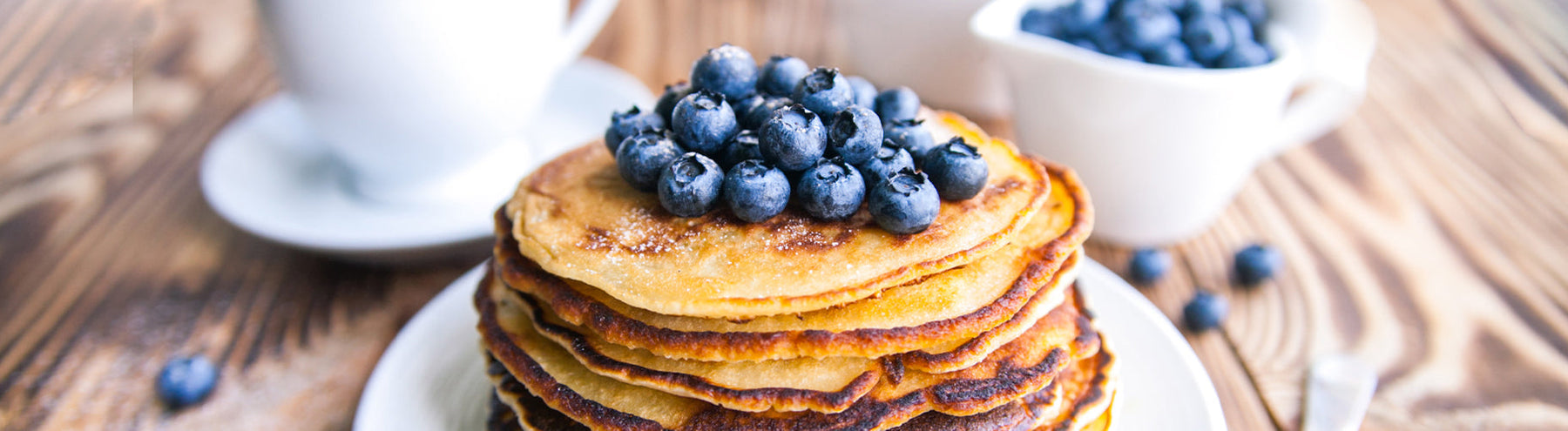 Stack of golden protein pancakes topped with fresh blueberries on a wooden table.