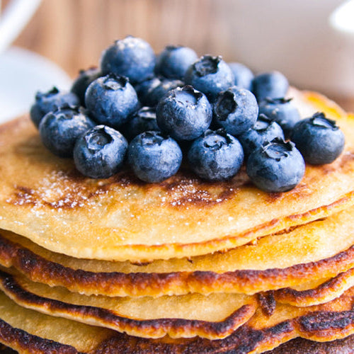 Stack of golden protein pancakes topped with fresh blueberries on a wooden table.