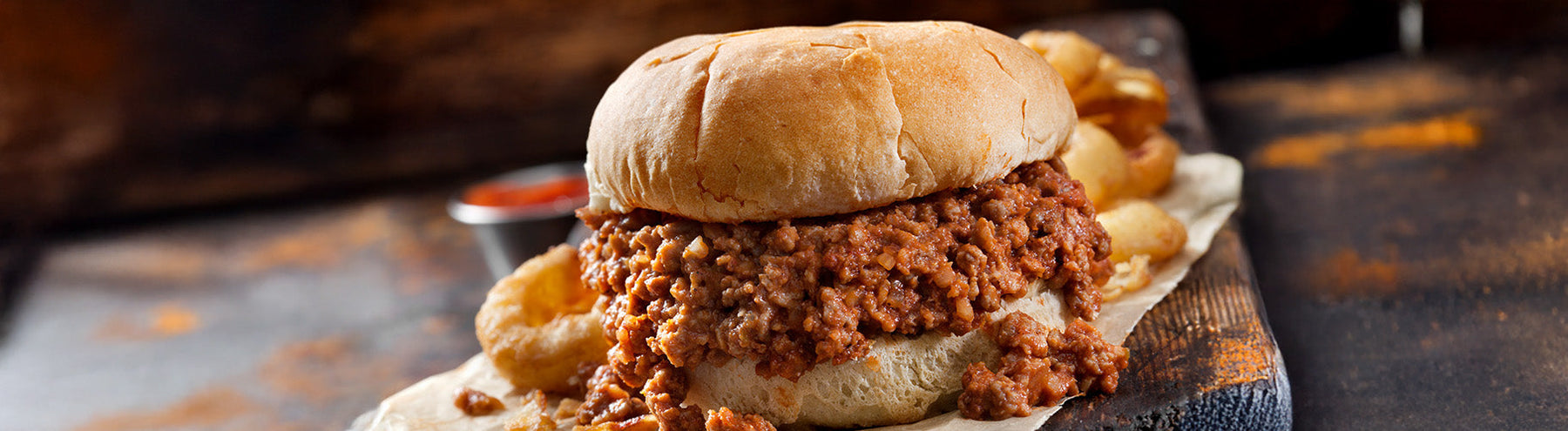 Sloppy joe sandwich with seasoned ground meat on a bun, served with fries on a wooden surface.