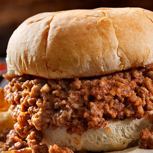 Sloppy joe sandwich with seasoned ground meat on a bun, served with fries on a wooden surface.
