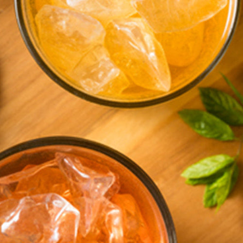 Iced fruit beverages with ice, lemon slices, berries, and fresh mint arranged on a wooden serving board.