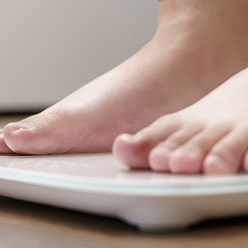 Close-up of a woman’s bare feet standing on a digital bathroom scale during.