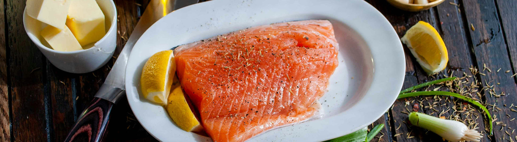 Plate of salmon with lemon slices, with a small cup of cubed butter off to the left side.