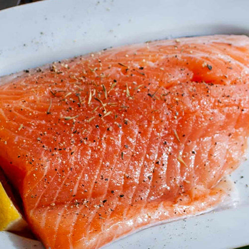 Plate of salmon with lemon slices, with a small cup of cubed butter off to the left side.